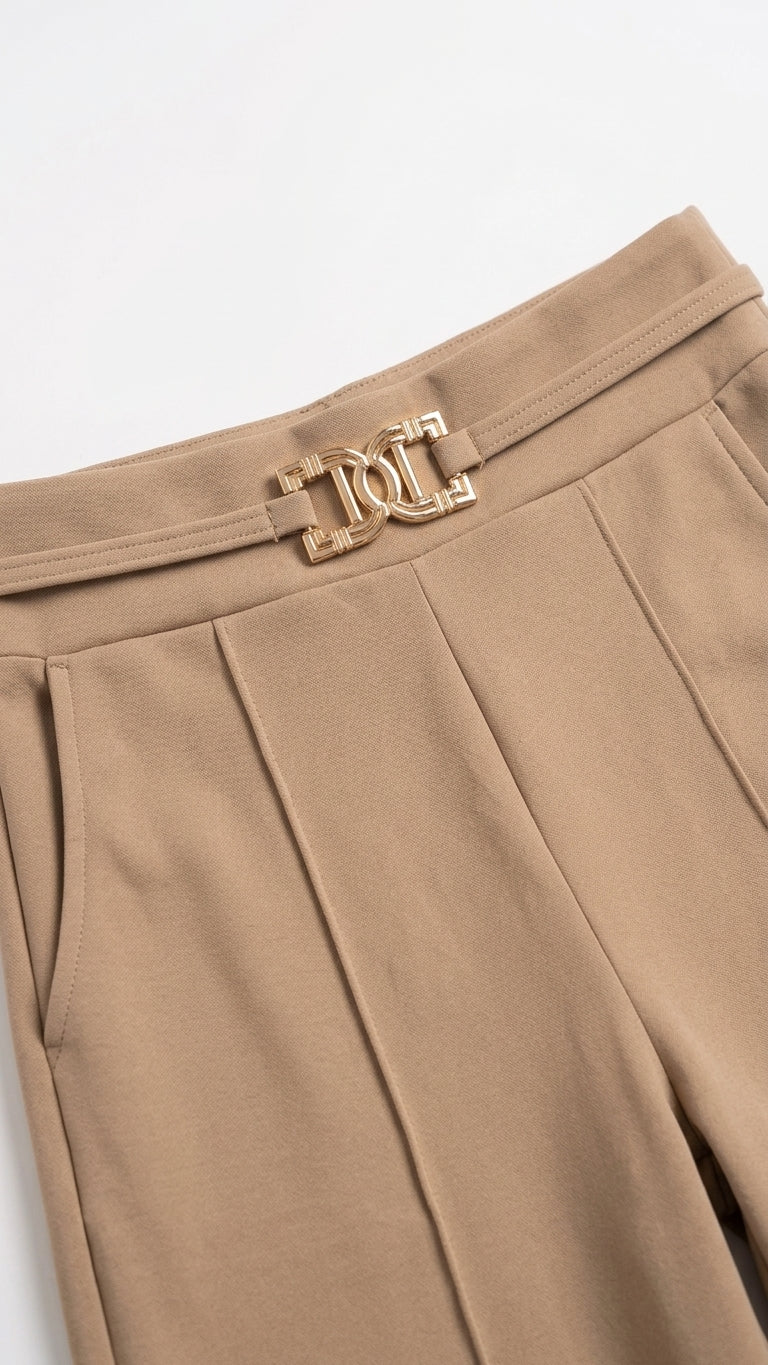 Close-up of beige pleated trousers featuring a decorative gold-tone metal belt buckle with an interlocking 'D' and 'L' design.