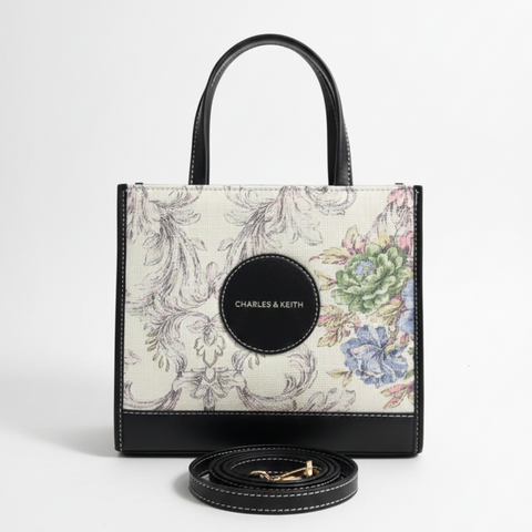 Designer handbag with floral pattern and matching round wallet on a light gray background